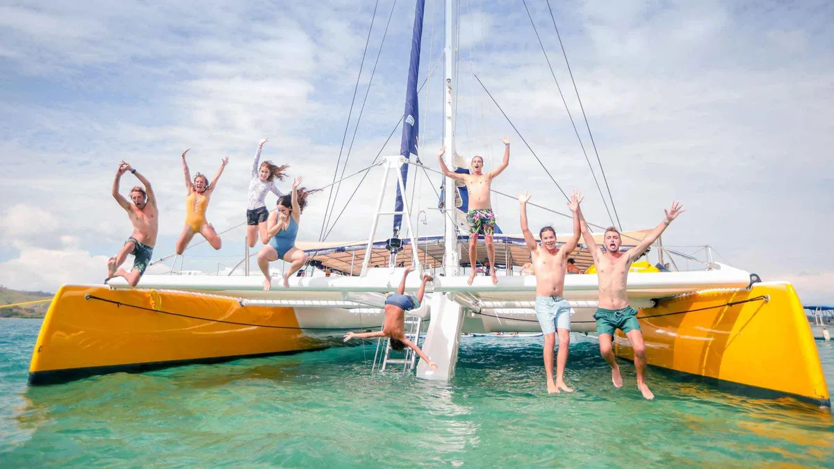 Guests jumping from the yellow Sabre sailing catamaran on a full-day Mamanuca Islands tour in Fiji